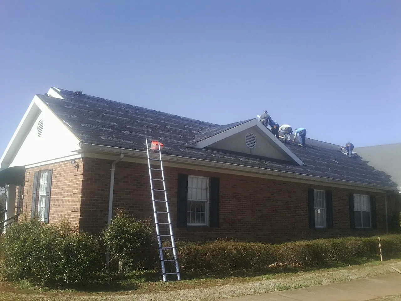 Crew tearing shingles off a brick ranch roof with a ladder set — Emergency Roof Repair work by our crew in East Lyme