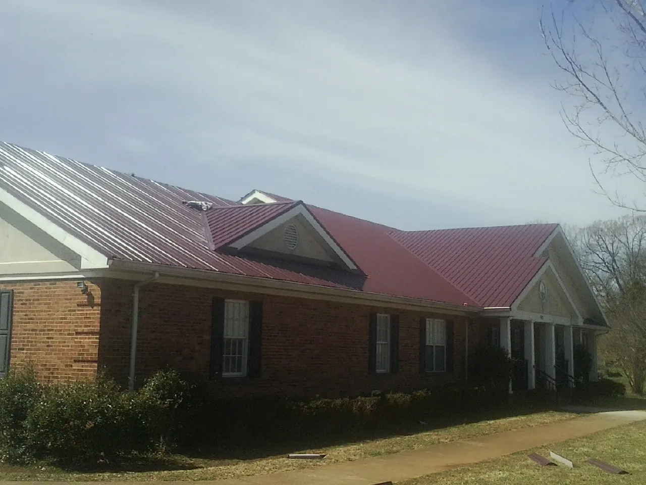 Red metal roof with gabled entries on a long brick building, from a Hail Damage Roof Repair job in East Lyme