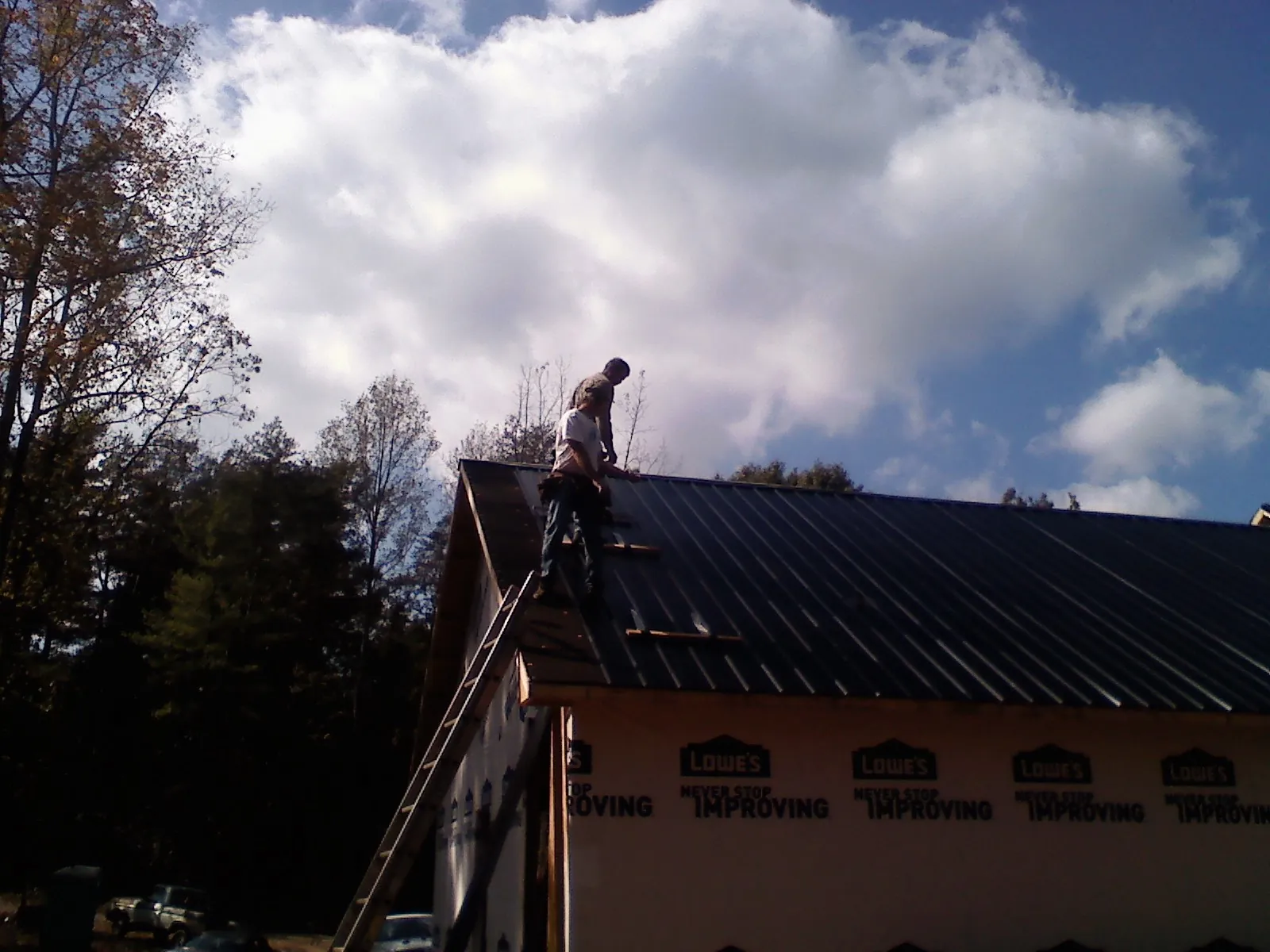 Roofer fastening dark metal panels high against a cloudy sky, from a Roof Inspection job in East Lyme
