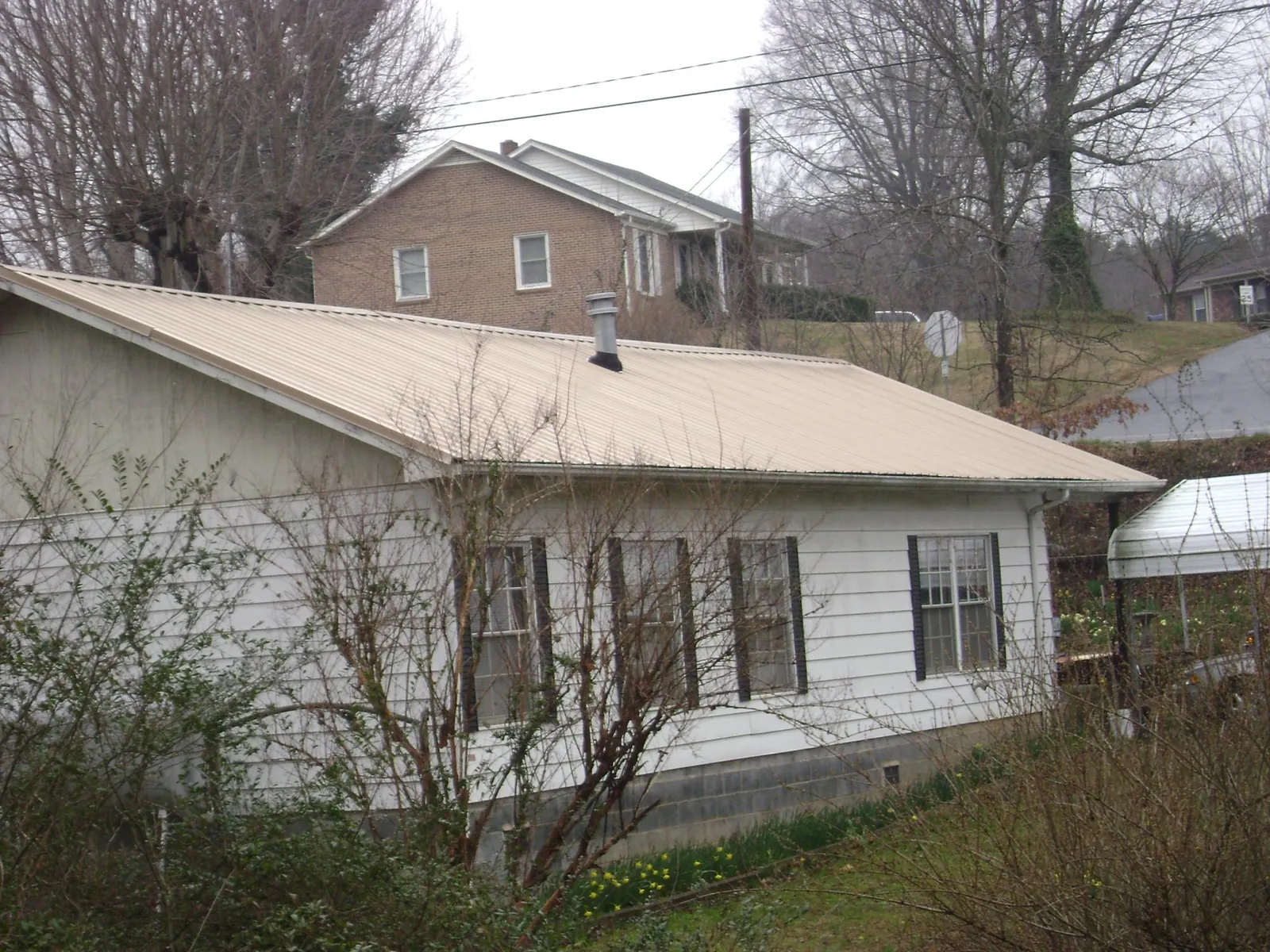 Tan metal roof on a white sided house set into a hillside — Commercial Roofing by Roofing Brothers in East Lyme